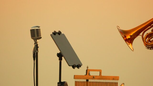 Instrument equipment setup featuring vintage microphone, tablet, chimes, and shiny cornet during golden hour. Static medium shot.