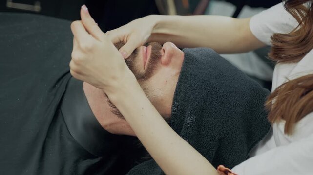 Barber applies lotion to a male clients beard during a professional grooming treatment in a barbershop.