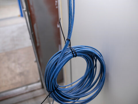 A neat coil of blue cable hangs from a tiewrap against a pale panel wall, ready for connection.