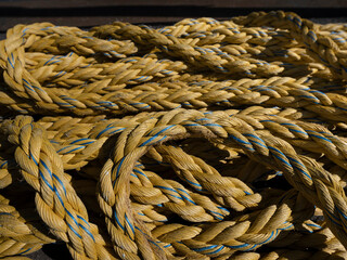 A thick yellow mooring rope with blue tracer threads lies coiled in hard sunlight, braided fibre in close detail. © Victor