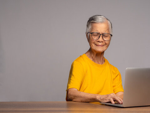 Senior woman using laptop at table and smiling at camera