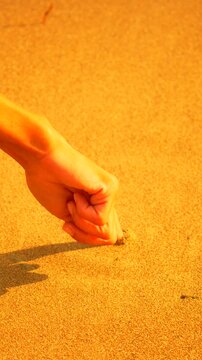 Hand drawing spiral shape in golden sand on beach during sunset. Vertical closeup shot.