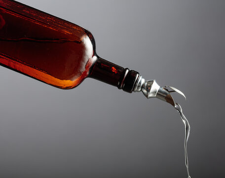 Antique dark brown glass bottle with vintage pourer on a gray background.