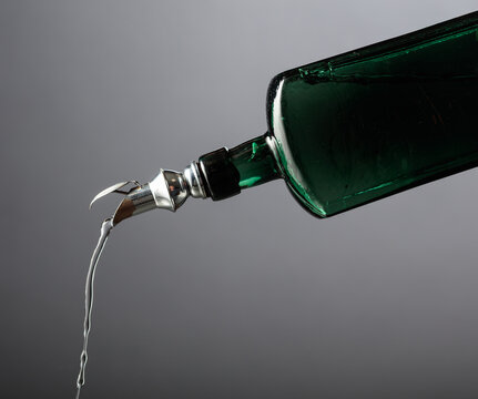 Antique dark green glass bottle with vintage pourer on a gray background.