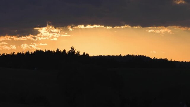 Panoramic landscape view captured during sunset as warm sky gradients illuminate the horizon above darkened tree lines and rolling terrain