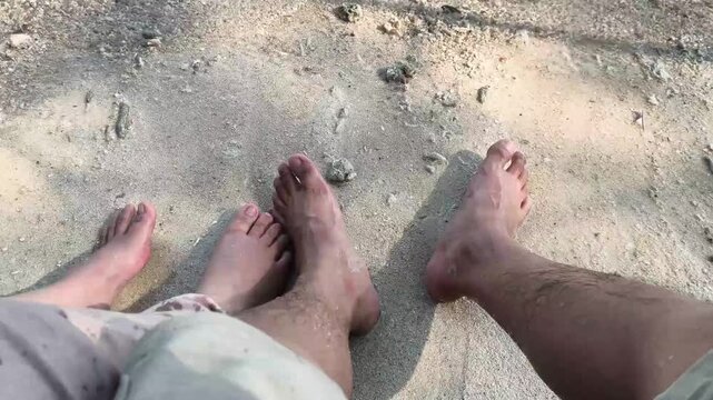 Jakarta, Indonesia - April 24, 2026: Bare feet of two people relaxing sitting on beach sand