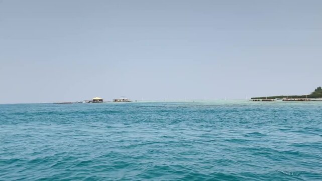 Calm blue sea horizon with distant tropical island under clear sky