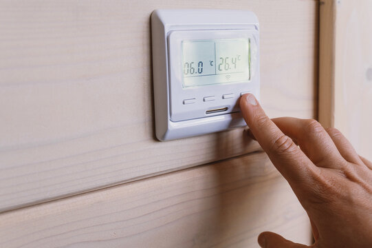 Female hand operates digital wall thermostat to adjust heating temperature, manage indoor comfort and improve household energy efficiency
