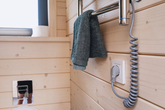An electric towel warmer is plugged into a wall outlet in a hotel bathroom featuring wood paneling. Energy efficiency, smart resource use, energy-efficient home, climate control.