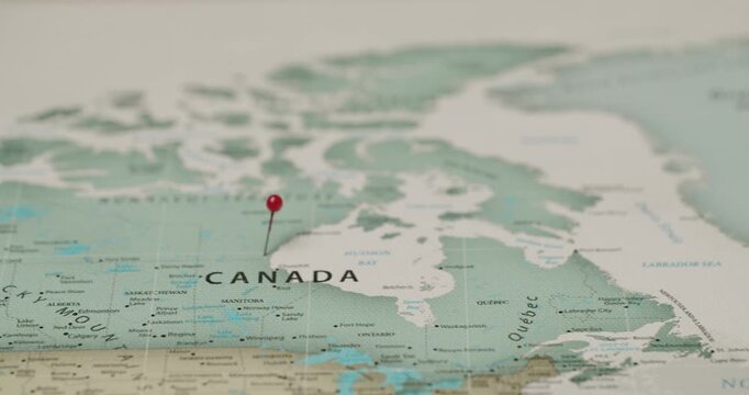 Close-up shot of a red pushpin marking the country of Canada on a vintage-style paper map, symbolizing travel planning, a destination point, or international relations and geography