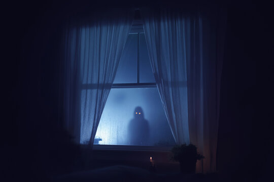 A ghostly figure with glowing eyes stands behind the curtains of an open window in a bedroom at night
