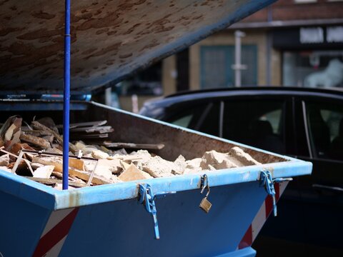 Large blue industrial skip container overflowing with concrete rubble and demolition waste locked with a brass padlock on a city street