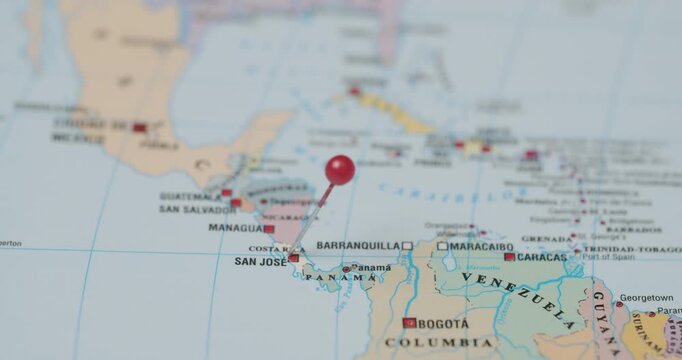 Person's hand sticking a red pin into Costa Rica on a world map, marking the capital city San Jose as a travel destination for an upcoming vacation or journey in Central America