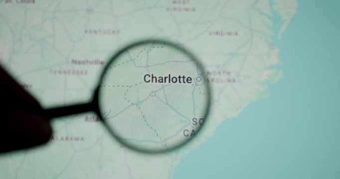 Person uses a magnifying glass to inspect a digital map on a screen, focusing on the city of Charlotte, North Carolina, enhancing the concept of travel planning and detailed exploration