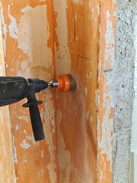 Rotary Hammer Drilling Wall with Core Bit for Electrical Socket Installation. Close-up of a worker using a rotary hammer drill with a large core bit to make a circular opening in a wall for an electri