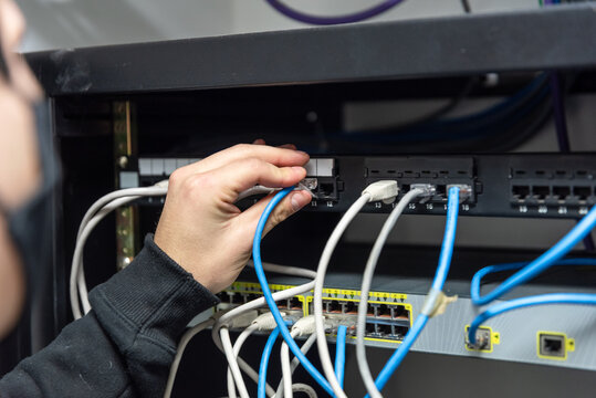 IT technician hand plugging ethernet network cable into server rack patch panel