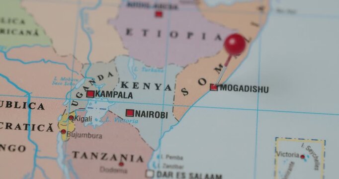 Close-up view of a person's hand placing a red pushpin on the city of Mogadishu, the capital of Somalia, on a colorful political map, marking it as a travel destination or point of interest
