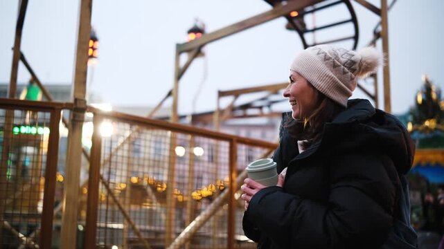 Happy Woman Walking At A Bright Illuminated Christmas Market Among Children's Roller Coasters And Attractions