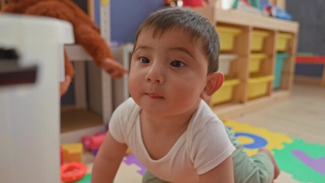 Boy holding red and blue plastic block to mouth while steadying hand on clear toy bin in classroom; curiosity discovery play.