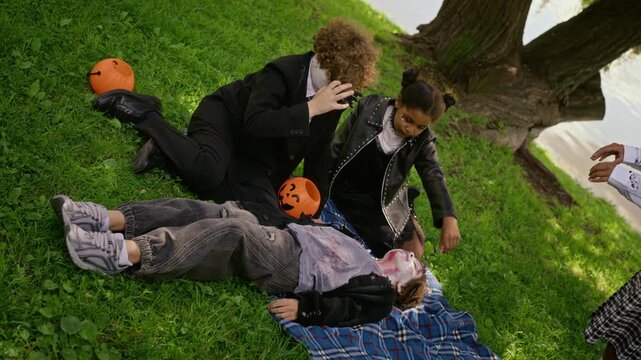 Diverse teenagers in Halloween makeup acting out zombie scene outdoors, high angle slow motion. Footage suitable for seasonal marketing, holiday campaigns, youth entertainment advertising