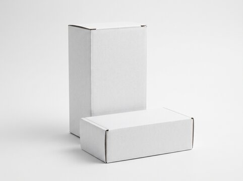 High angle view of two blank white cardboard boxes with one standing upright and one lying horizontal isolated on white background. Product packaging box mockup.