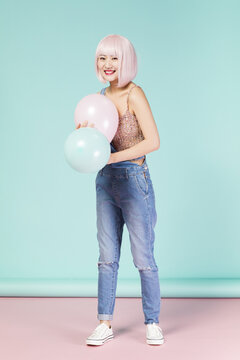 Happy young woman with pink hair holding pastel balloons in a studio