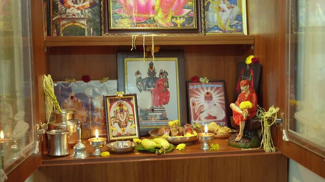 Slow motion view of a South Indian home pooja cabinet filled with Hindu deity photos, lamps, fruits, and flowers arranged for worship.