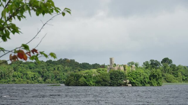 Wide lakeside view of McDermott's Castle on wooded Castle Island across Lough Key, a historic Irish landmark in County Roscommon surrounded by dense greenery.