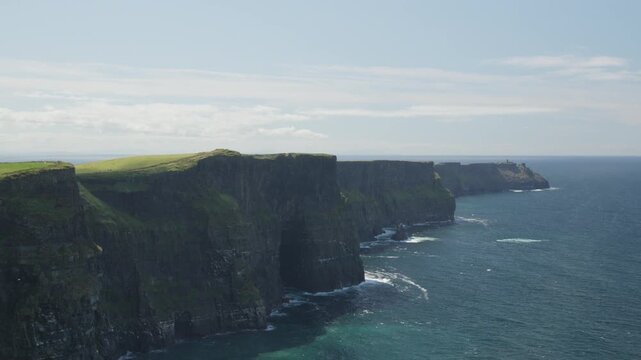 Long coastal view of the Cliffs of Moher extending beside deep blue Atlantic water, with grassy tops and layered rock faces in County Clare, Ireland.