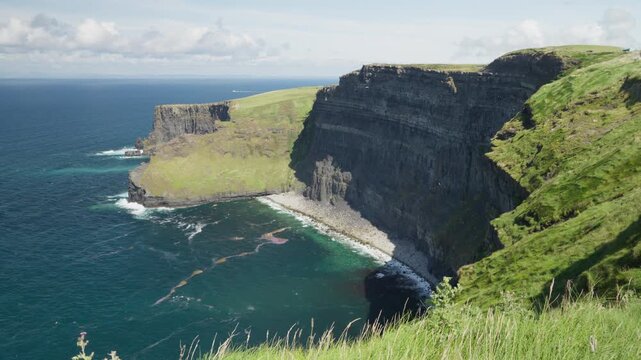 Wide view into a rocky inlet below the Cliffs of Moher, with layered rock walls, turquoise water and Atlantic surf along the County Clare coastline.