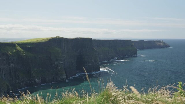 Wide view along the Cliffs of Moher, showing sheer layered rock walls, grassy tops and Atlantic water stretching along the County Clare coast in Ireland.