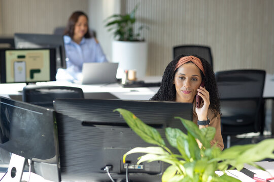 African American female coworkers talking on phone while working at open office desks with monitor