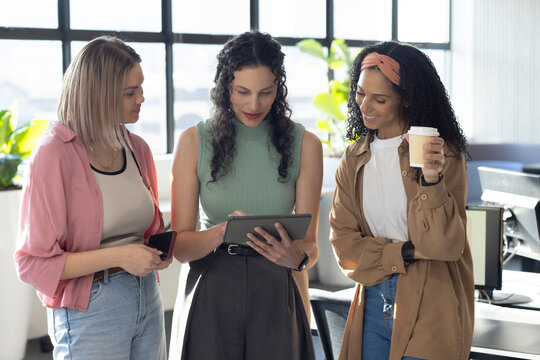 African American women gathering around tablet in open office holding phone and to-go cup