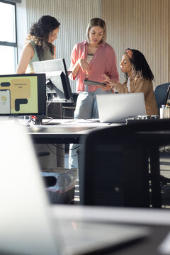 African American women reviewing tablet at modern office desk with laptops and monitor showing app