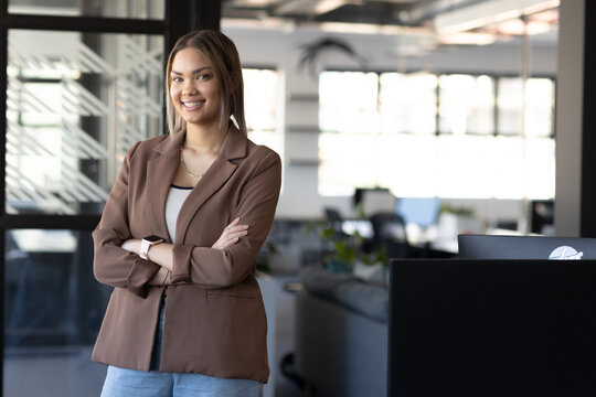 African American woman posing by frosted glass divider in office arms crossed in blazer, copy space