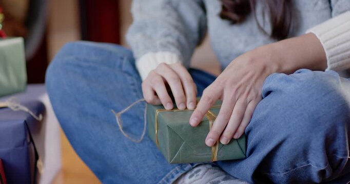 Wearing gray knit woman on floor untying twine on green gift finding tag inspecting reading sender