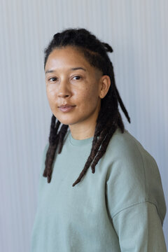 Non-binary person standing, facing camera in ribbed wall portrait with sage sweatshirt