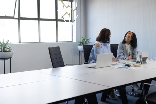 African American women reviewing charts on laptops in office wearing office attire, copy space