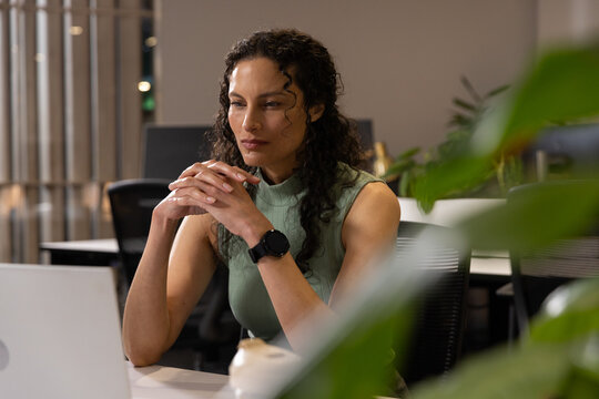African American woman sitting at desk in office using laptop, in green tank with smartwatch
