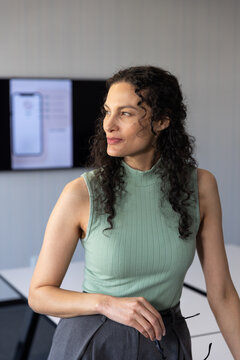 African American adult woman leaning on white table holding glasses wearing sage top facing monitor