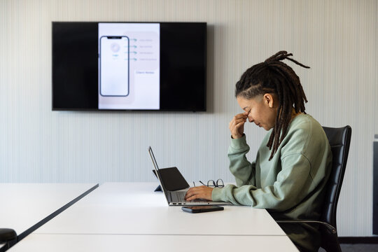 Non-binary African American sitting at table wearing green sweater with laptop, glasses, copy space