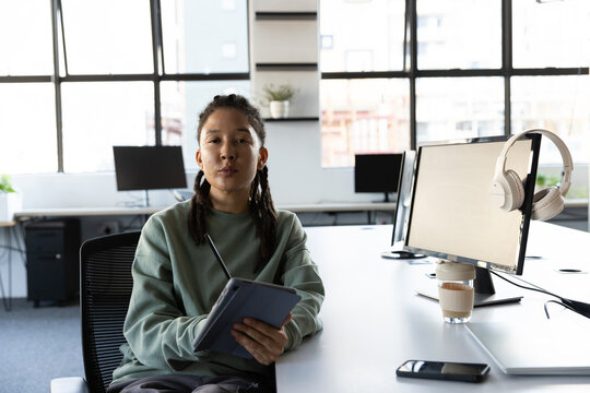 African American non-binary adult working on tablet and stylus at modern open-plan office