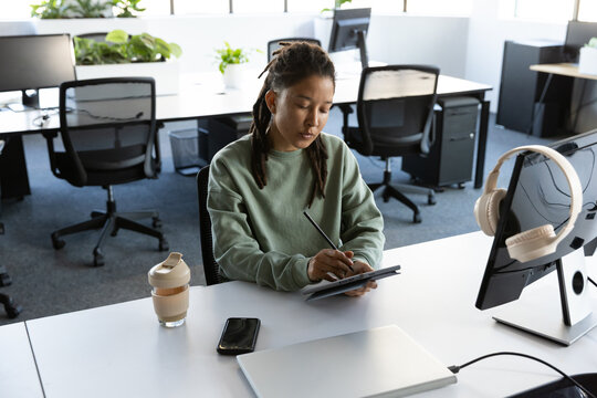 Nonbinary African American wearing green sweater sitting at open office desk using stylus on tablet