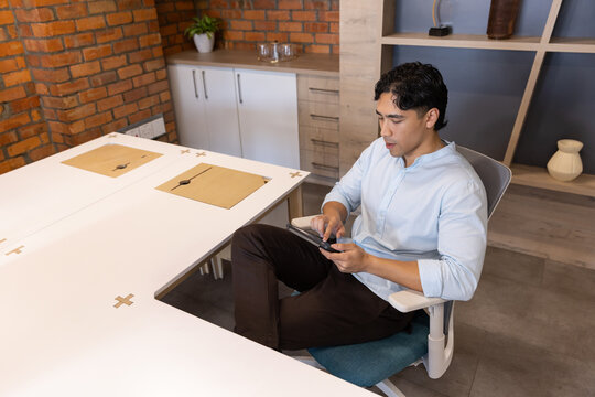 Asian man sitting in ergonomic chair at meeting table holding smartphone in blue shirt, copy space