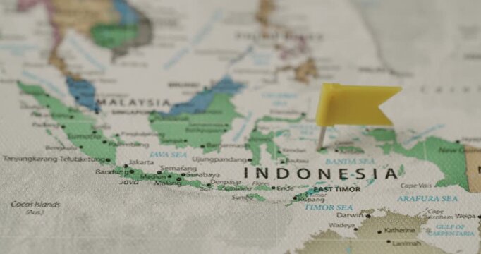 Traveler's hand placing a yellow flag pin on a map of Indonesia, marking a travel destination for vacation, adventure, or business, showcasing the concept of planning a journey