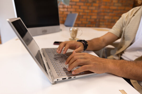 Asian adult male typing on silver laptop in casual workspace, wearing short-sleeve shirt
