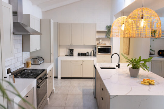 Kitchen island is anchoring modern kitchen scene with marble countertop, rattan pendants, bananas