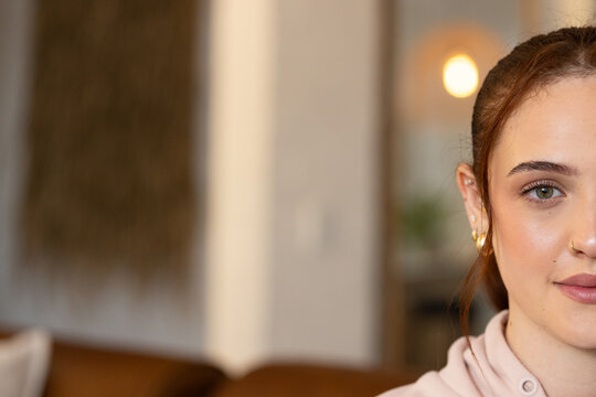 Right half woman's face is showing with hoop earrings, nose stud, pink pullover in living room
