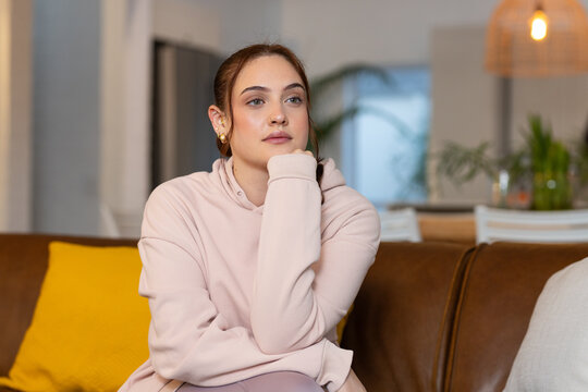 Woman sitting on brown leather sofa at home wearing pale pink hoodie and gold hoop earrings