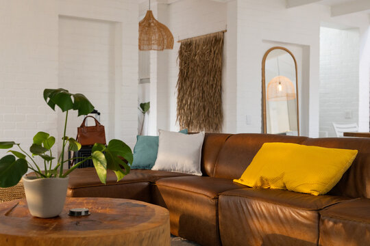 Brown leather sectional sofa is anchoring living room corner with yellow, teal, gray pillows, table